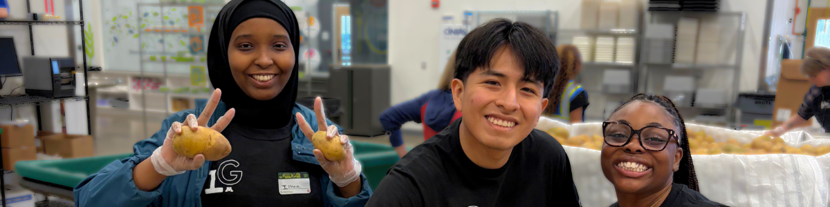 Three students pose while volunteering to pack produce at Second Harvest Heartland.