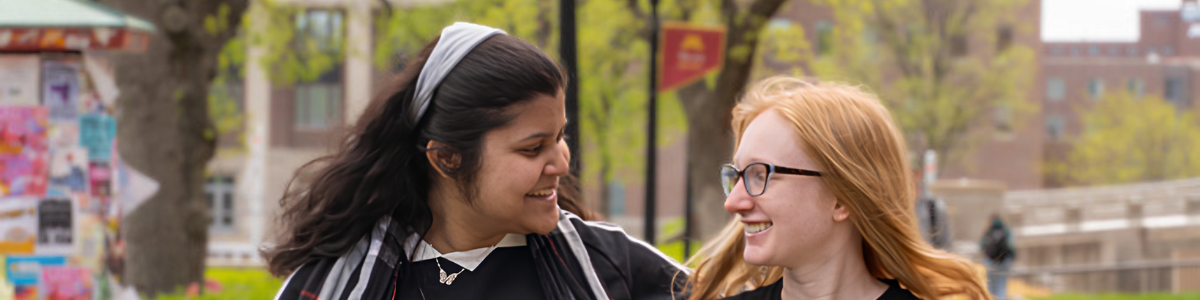 Two students walk along the East Bank mall, smiling and talking.
