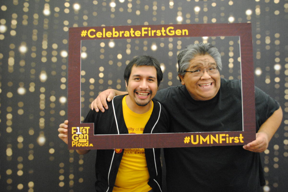 two staff members smiling together in a frame prop that says celebrate first gen